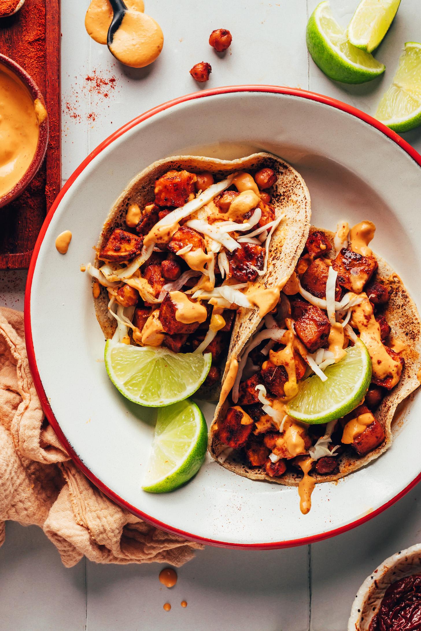 Two BBQ chickpea sweet potato tacos on a plate with cabbage and lime wedges