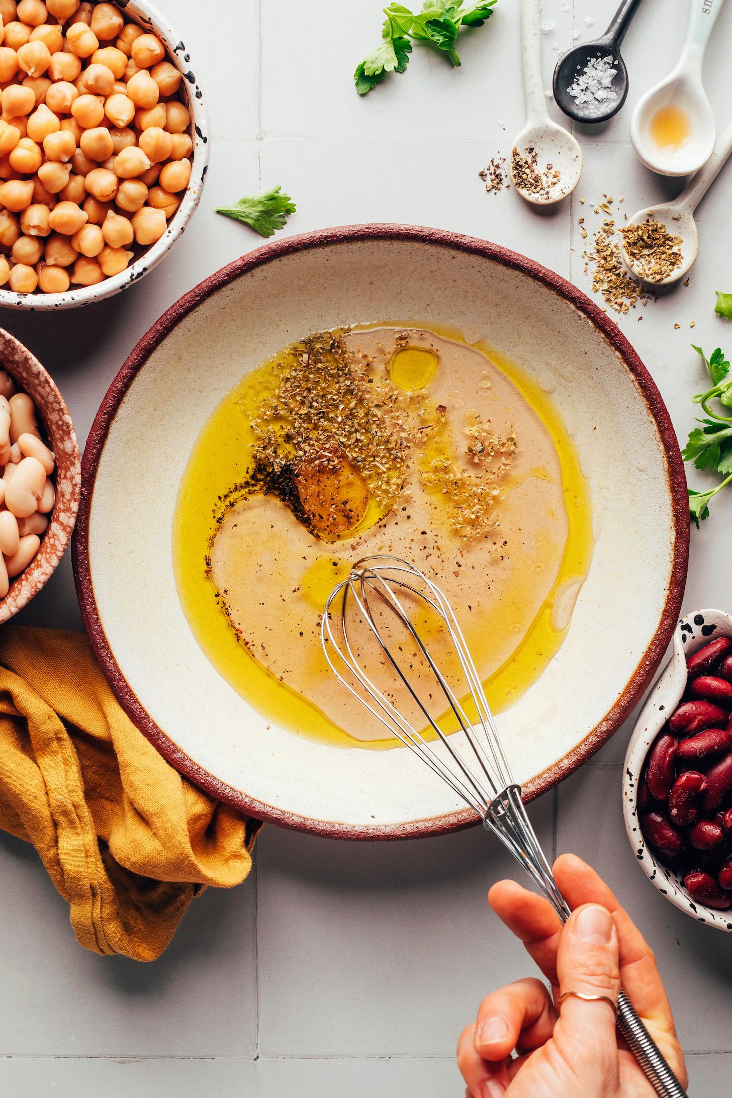 Whisking together olive oil, red wine vinegar, salt, pepper, and dried oregano