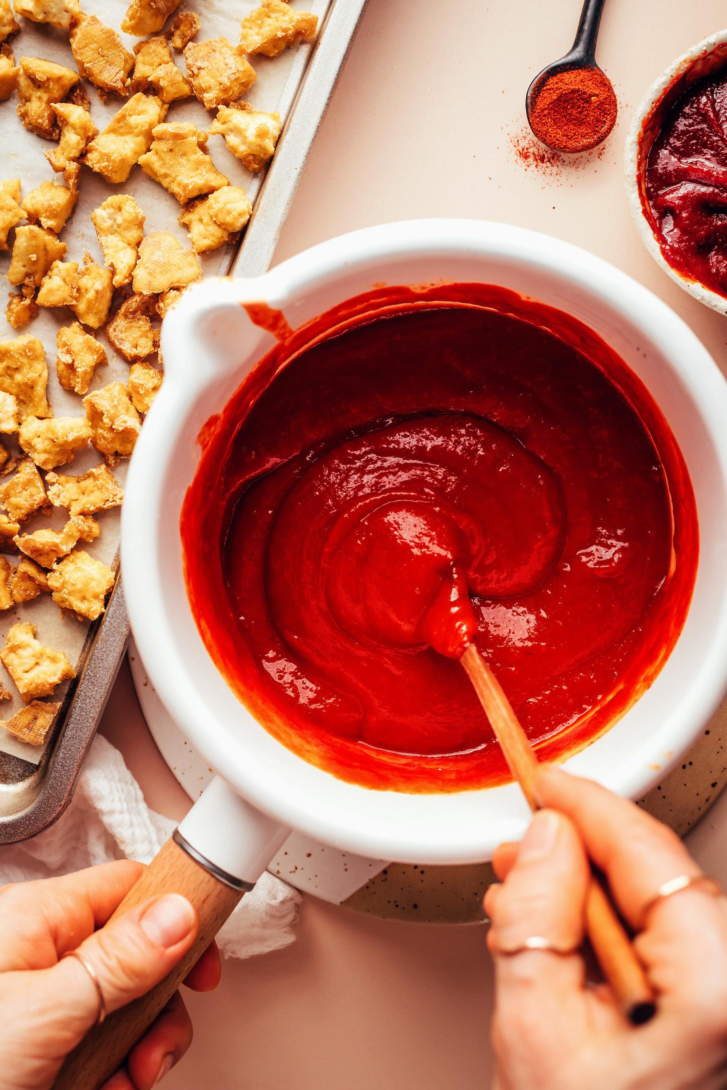 Stirring a Korean-inspired sauce in a saucepan next to a baking sheet of crispy baked crumbled tofu