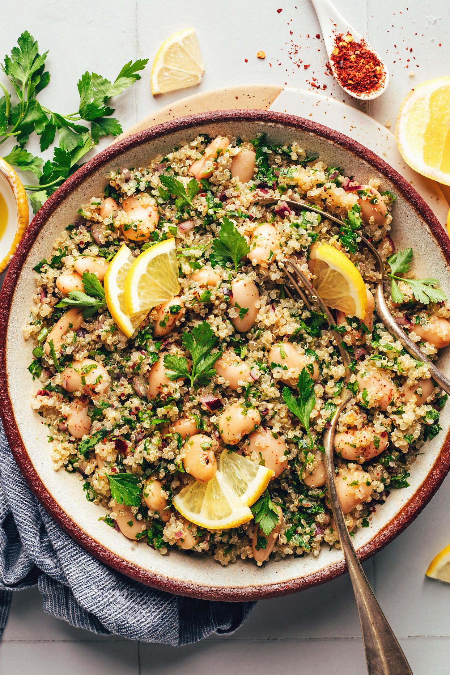 Fork and spoon in a bowl of white bean quinoa salad topped with lemon slices