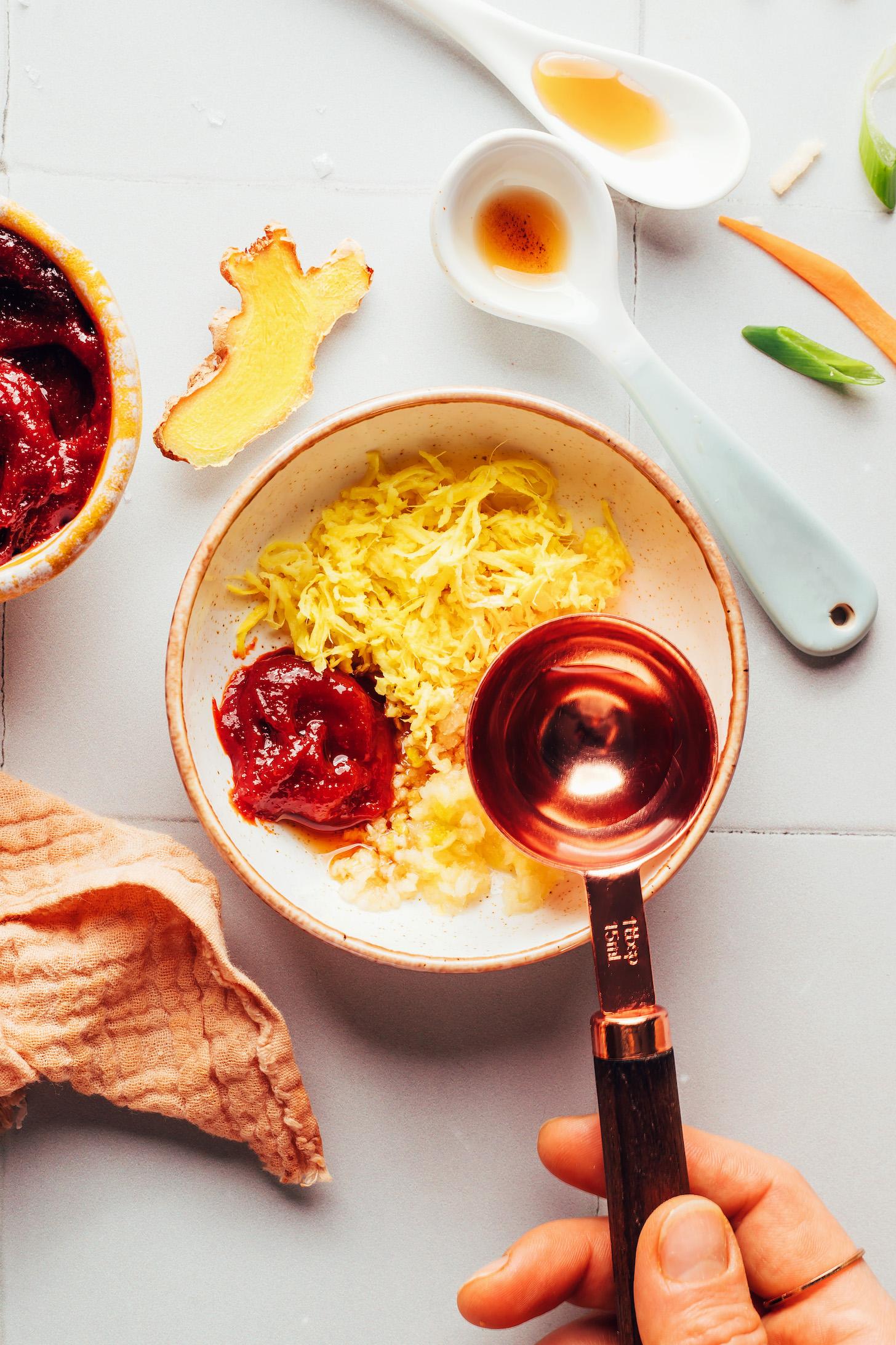 Pouring rice vinegar over grated ginger, garlic, and gochujang