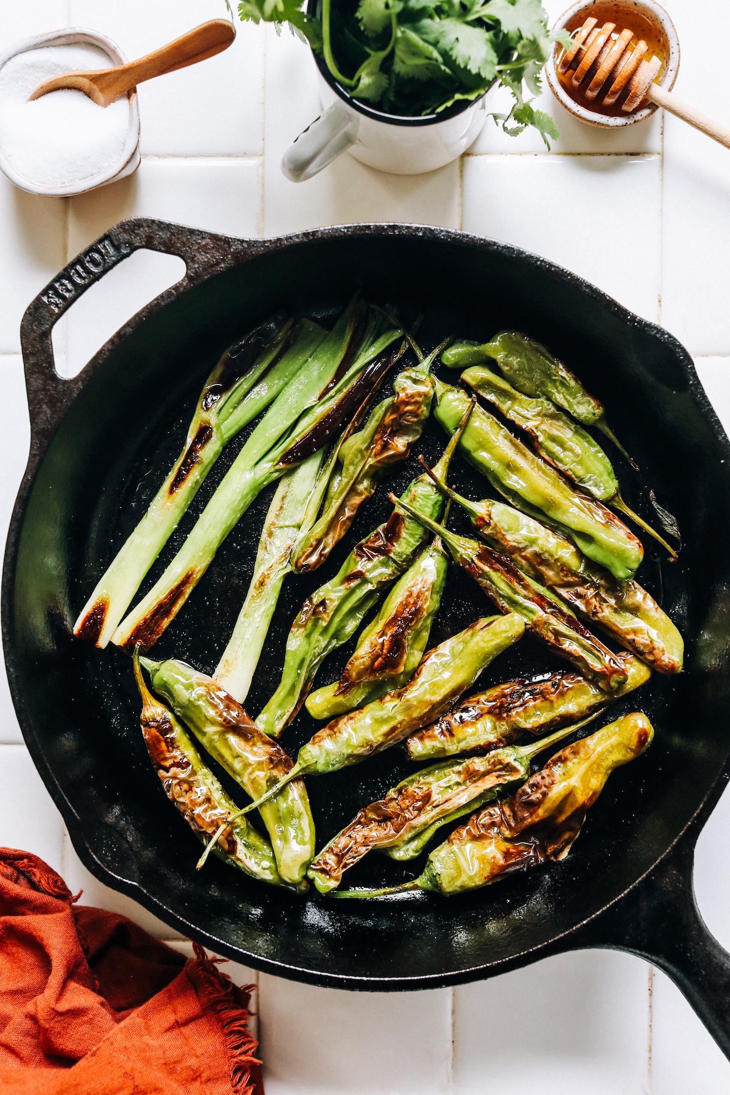 Charred shishito peppers and green onions in a cast iron skillet