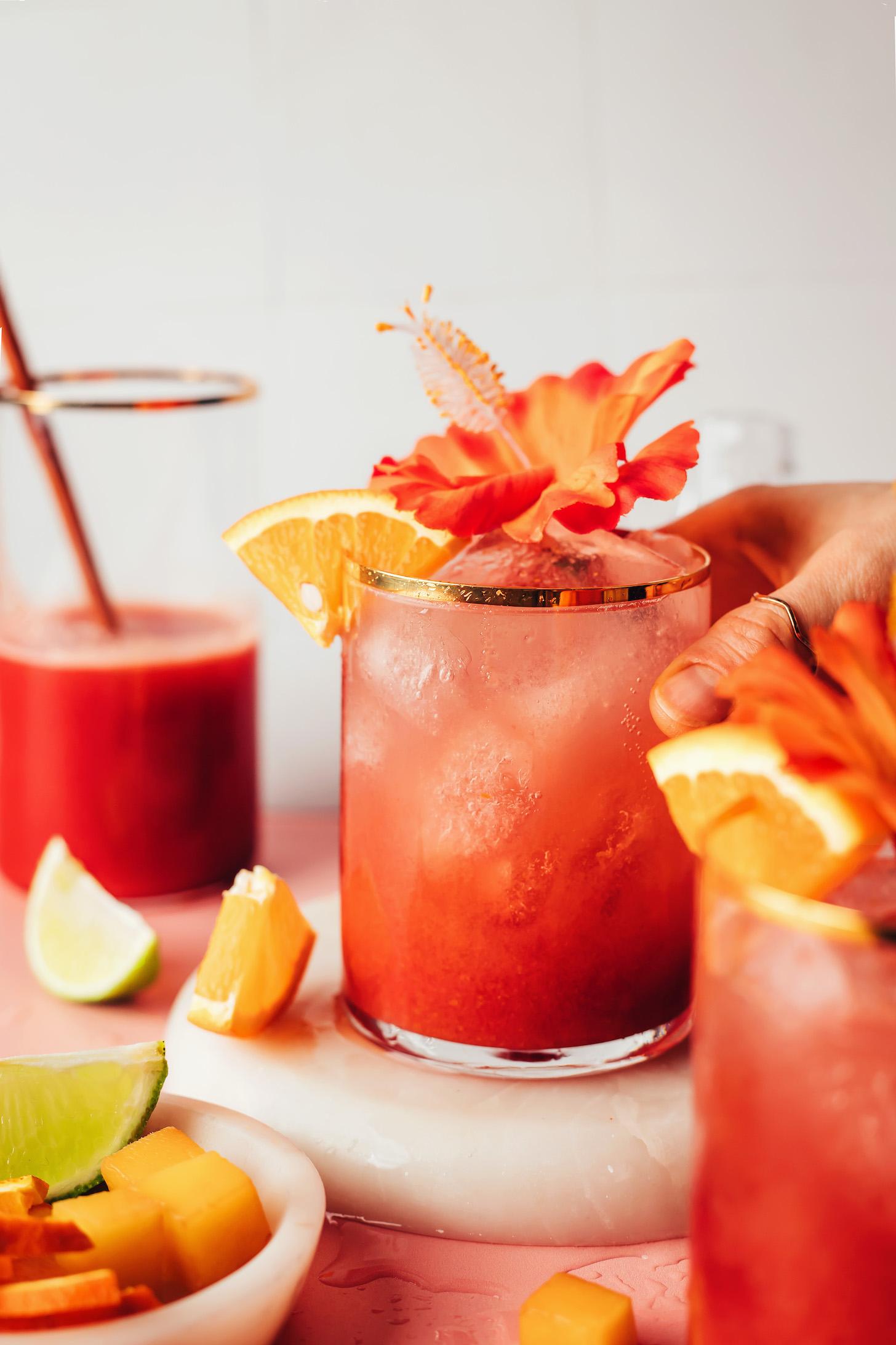 Hand reaching in to pick up a glass of our sparkling hibiscus orange mocktail recipe