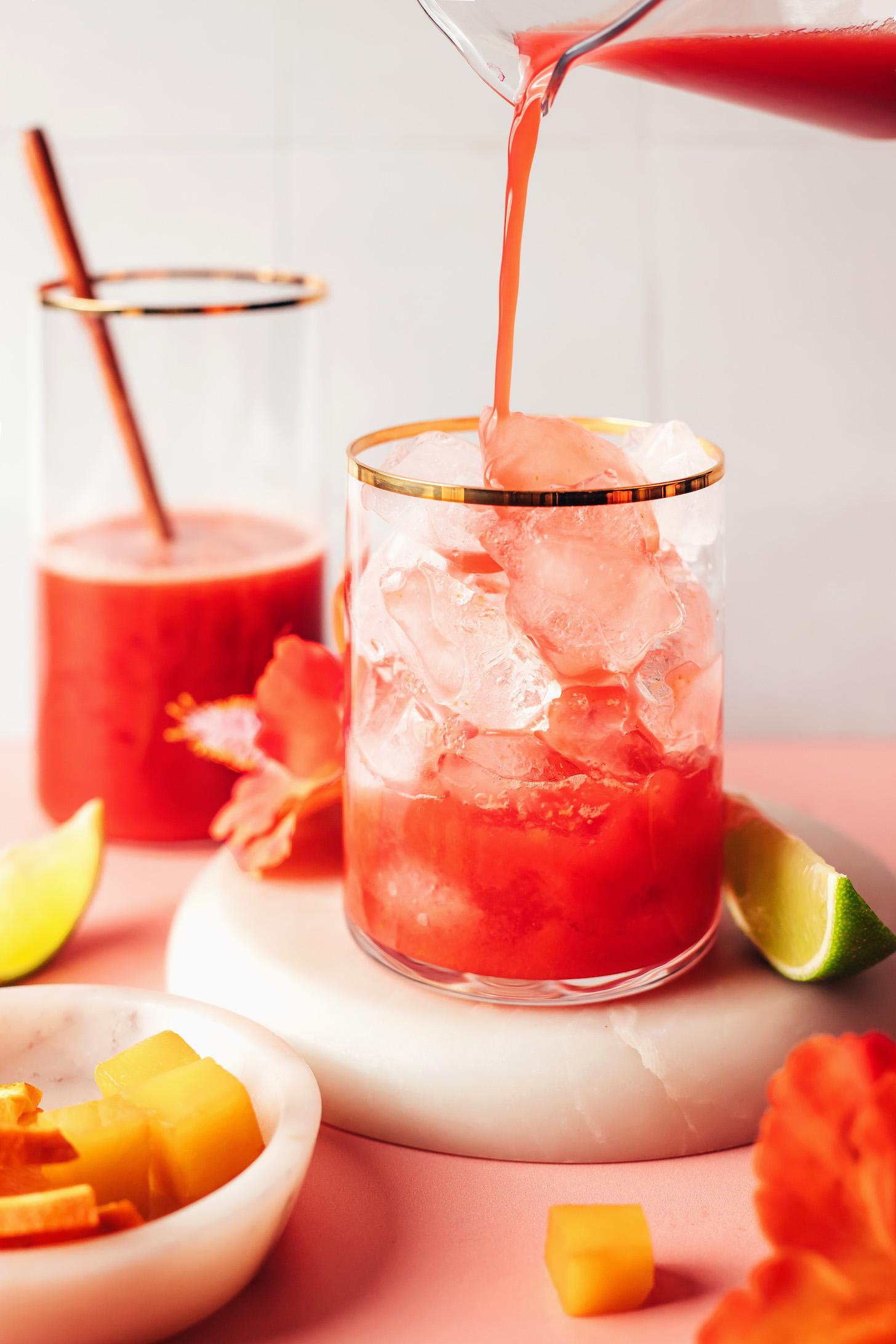 Pouring a hibiscus orange mango mixture over ice into a glass