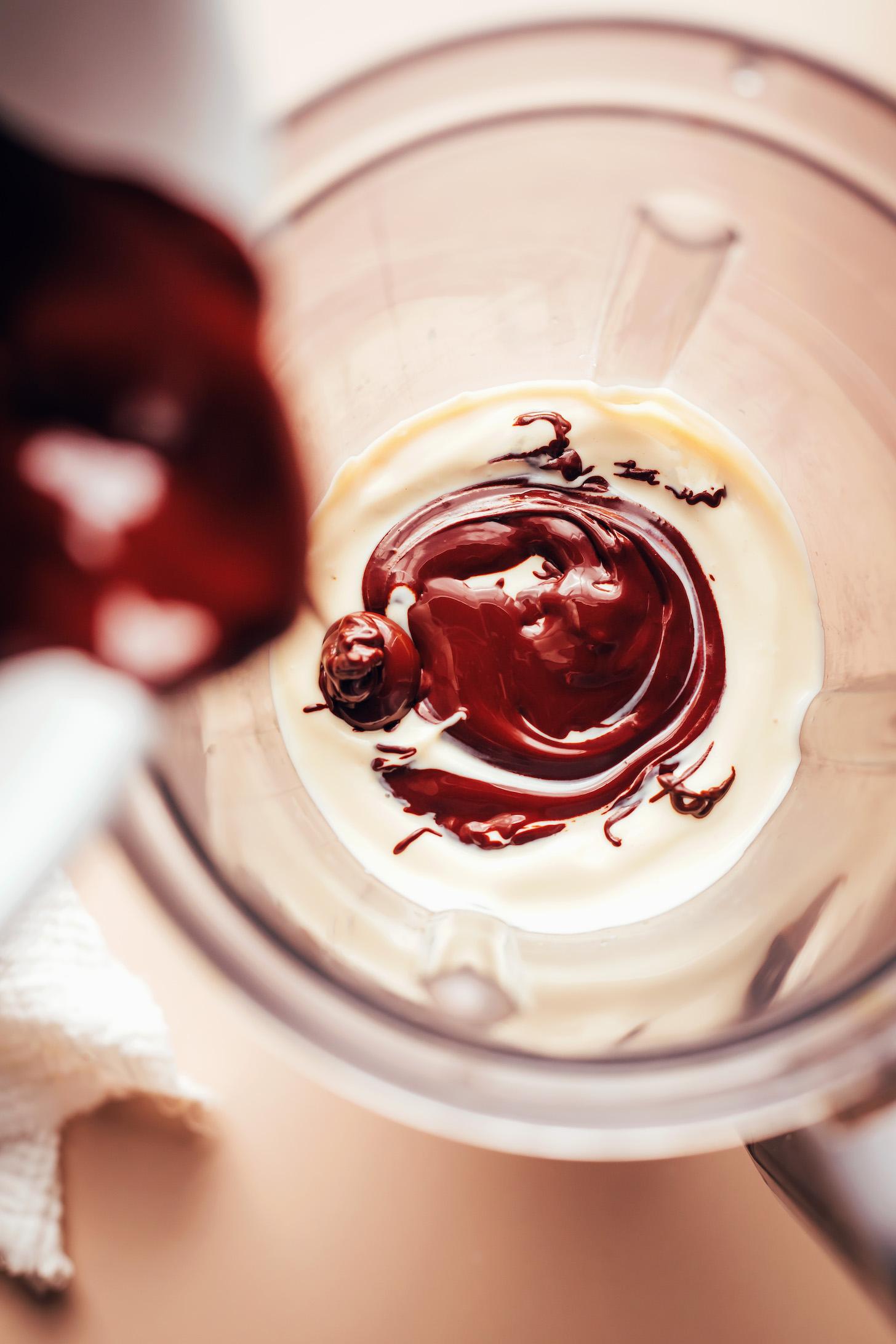 Pouring melted dark chocolate chips into a blender with creamy silken tofu