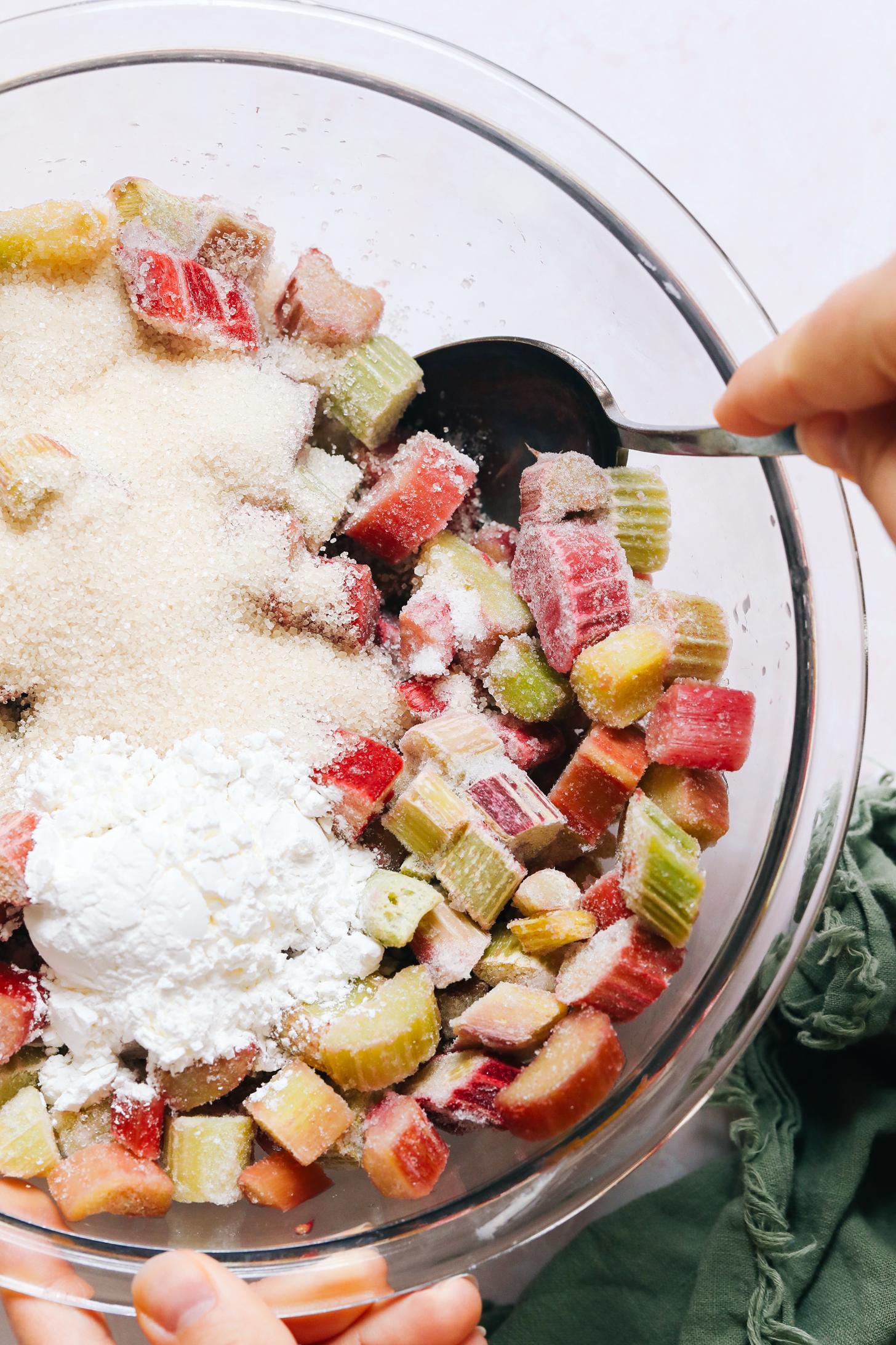 Using a spoon to stir together chopped rhubarb, cane sugar, and cornstarch