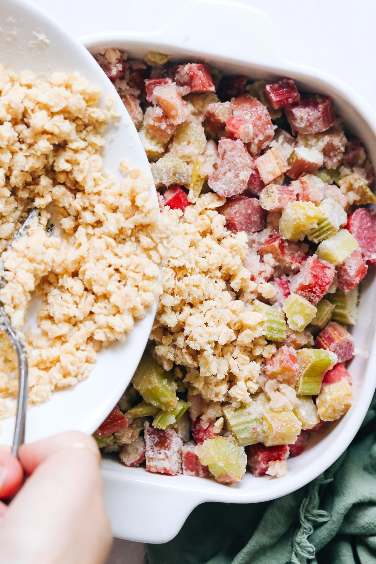 Adding an oat almond crisp topping over a rhubarb filling in a baking dish