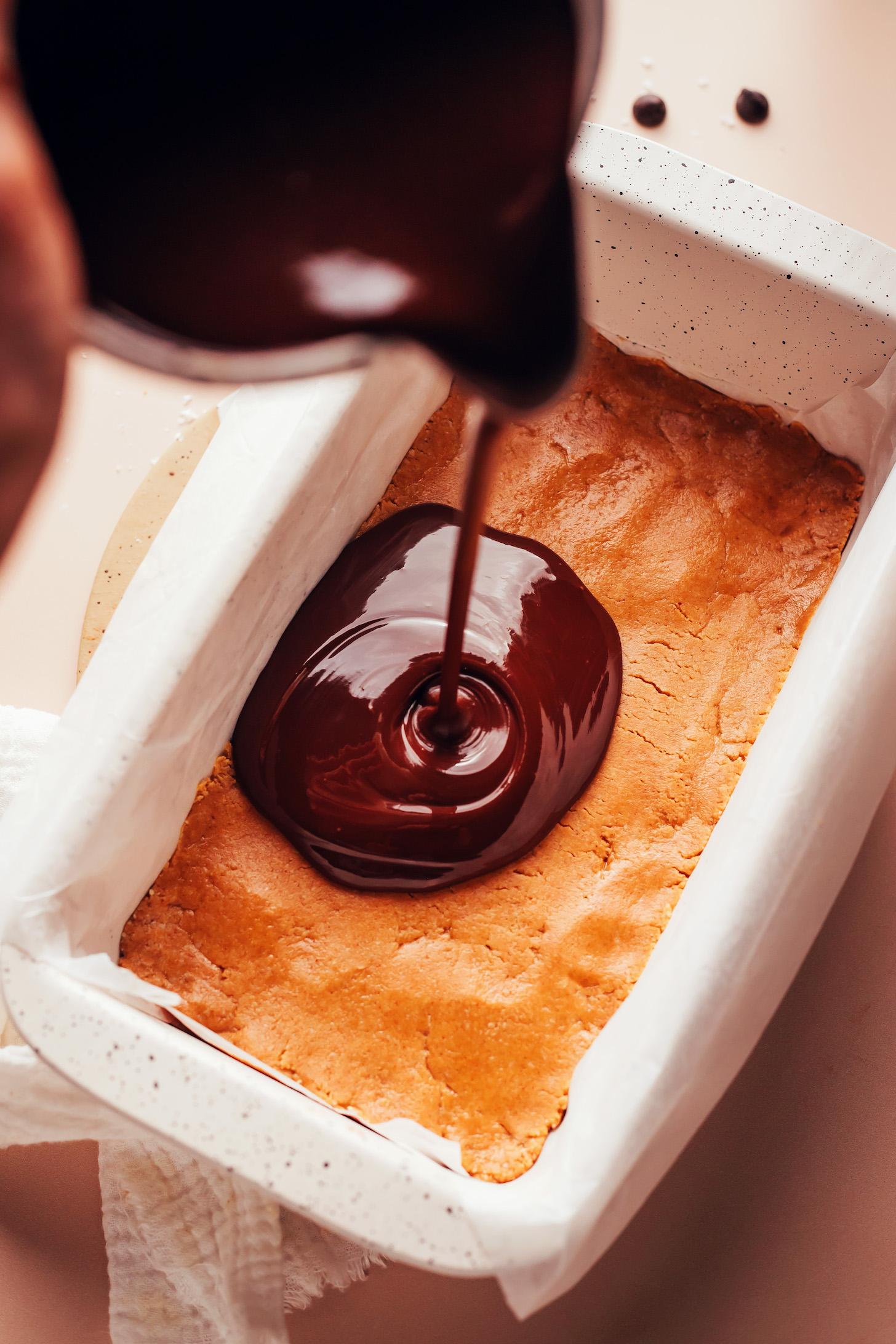 Pouring a melted chocolate mixture over a peanut butter base in a loaf pan