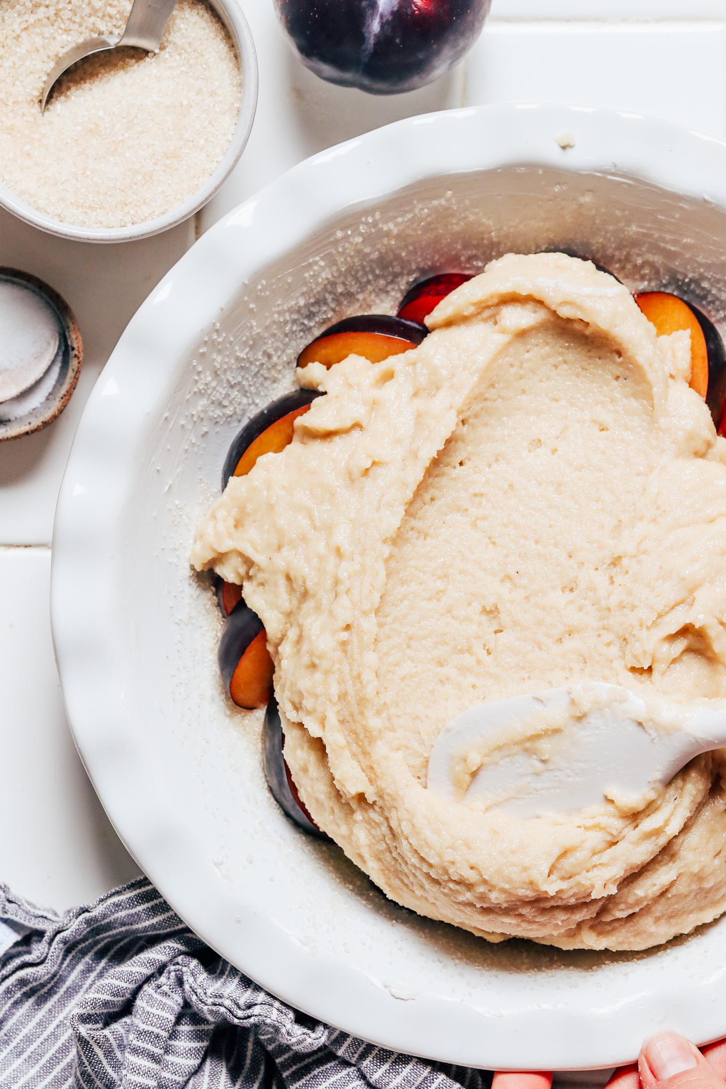 Spreading gluten-free almond cake batter over sliced plums in a pie pan