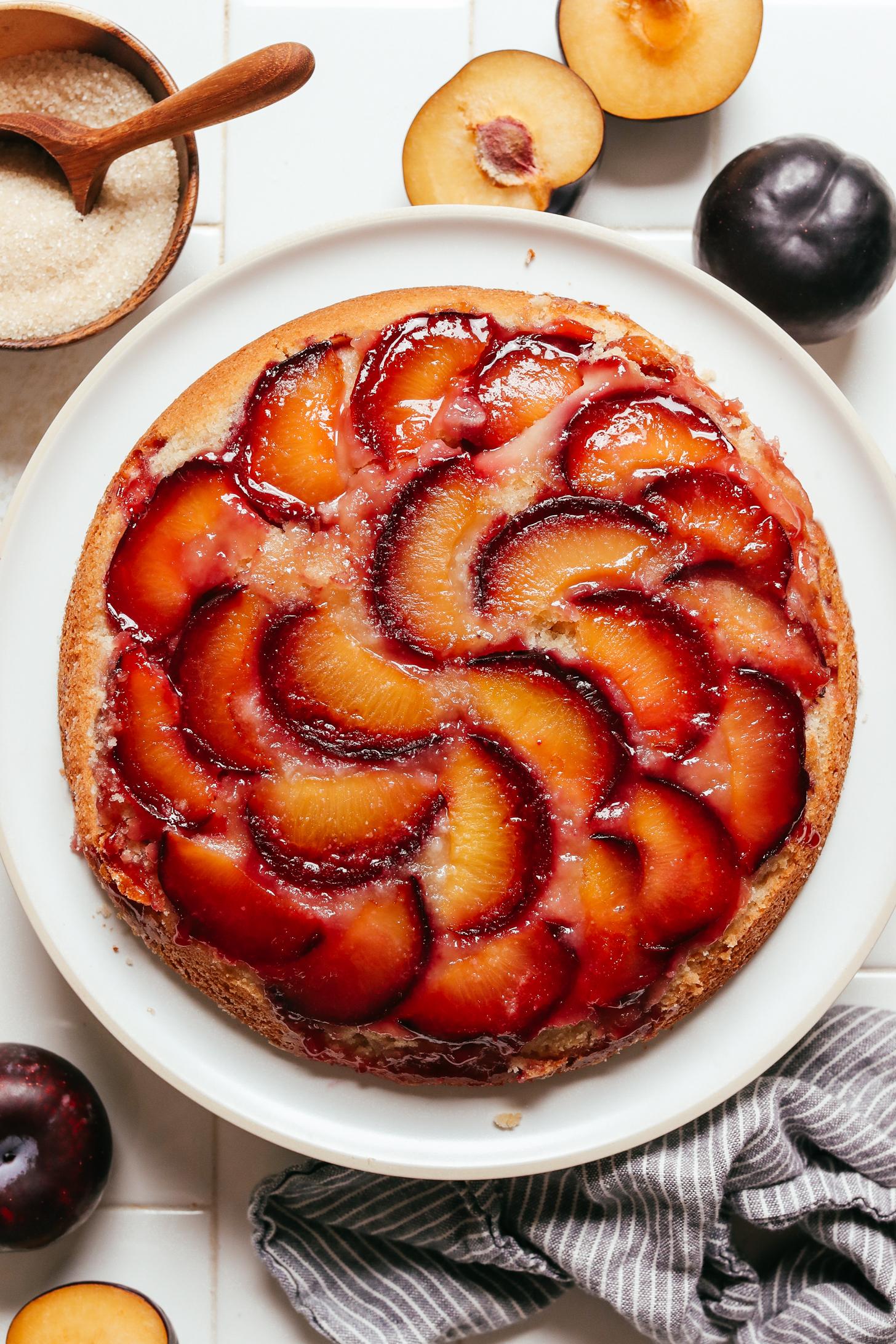 Black plums and cane sugar next to a plate of plum upside down cake