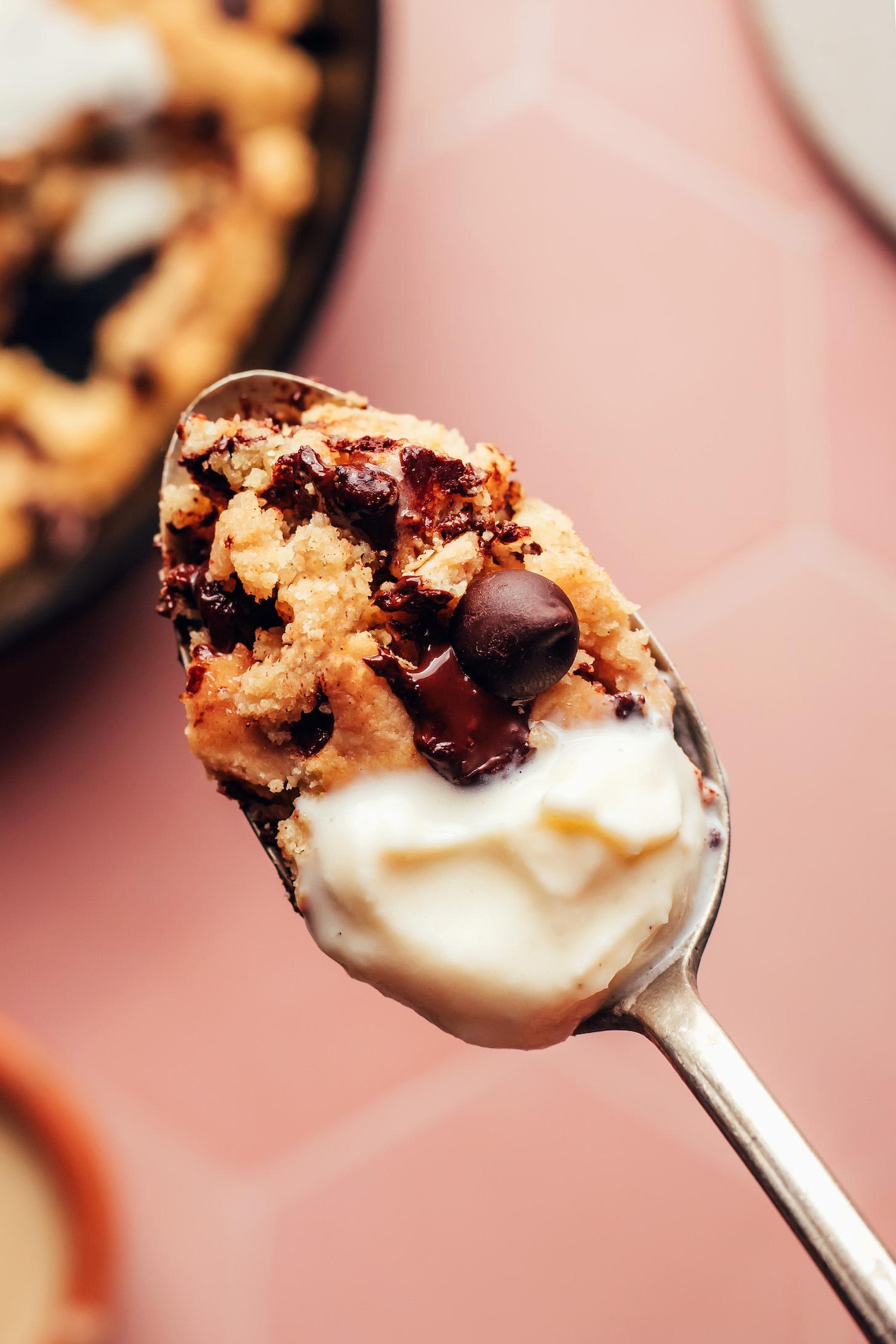 Close up shot of a spoon with a bite of chocolate chip skillet cookie and vanilla ice cream