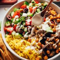 Drizzling tahini sauce over a Mediterranean nourish bowl