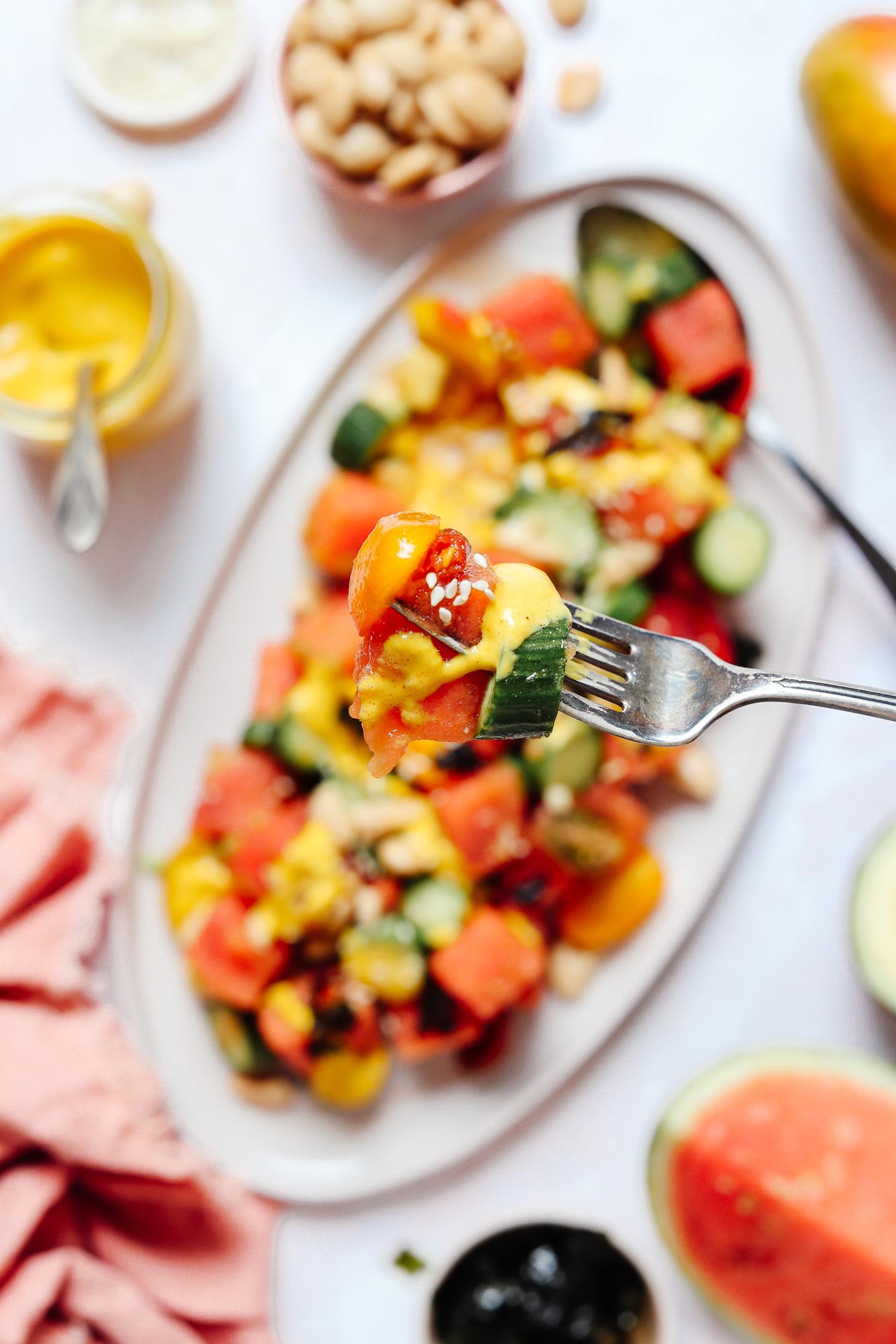 Fork with a bite of spicy watermelon salad over a platter of salad