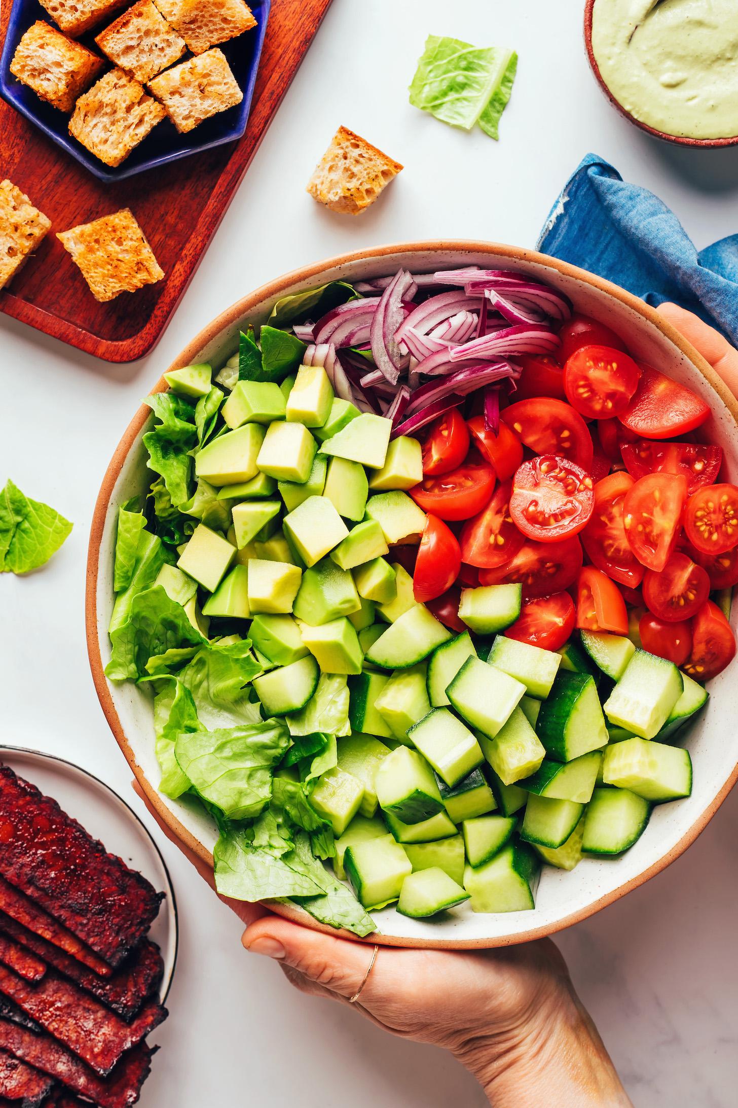 Holding a bowl of chopped romaine, cucumber, tomatoes, red onion, and avocado