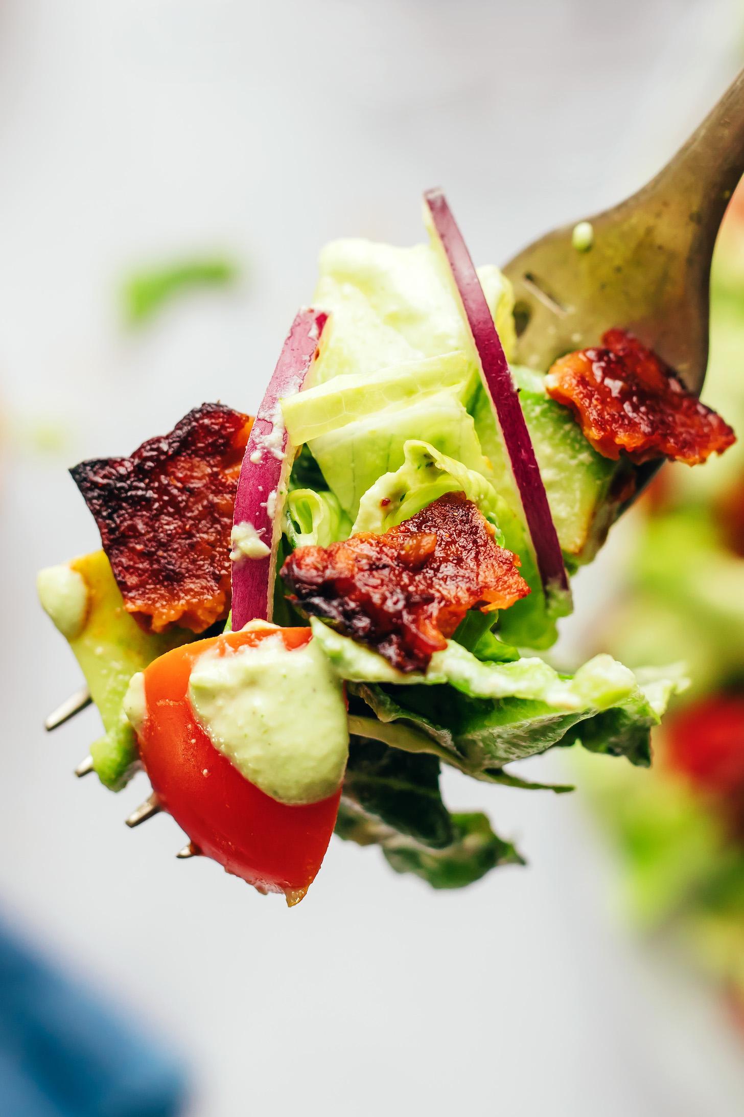 Close up shot of a fork spearing a bite with lettuce, cucumber, tempeh bacon, red onion, tomato, and ranch dressing