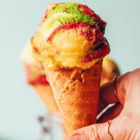 Holding an ice cream cone topped with homemade rainbow sherbet ice cream