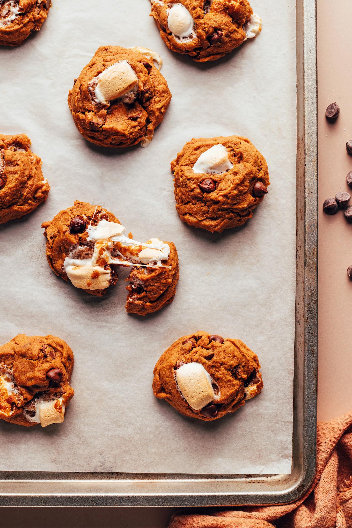 Baking sheet of s'mores cookies with one cookie partially separated to show the gooey, sticky marshmallows