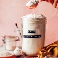 Picking up a spoonful of gluten-free flour blend from a jar