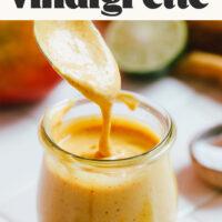 Mango salad dressing pouring off a spoon into a small jar