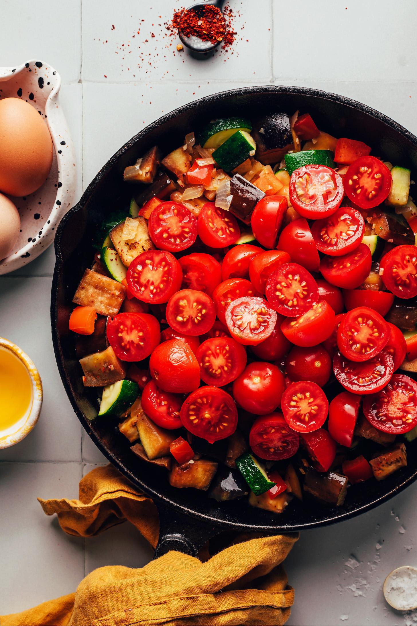 Cooking chopped eggplant, zucchini, and cherry tomatoes in a cast iron skillet