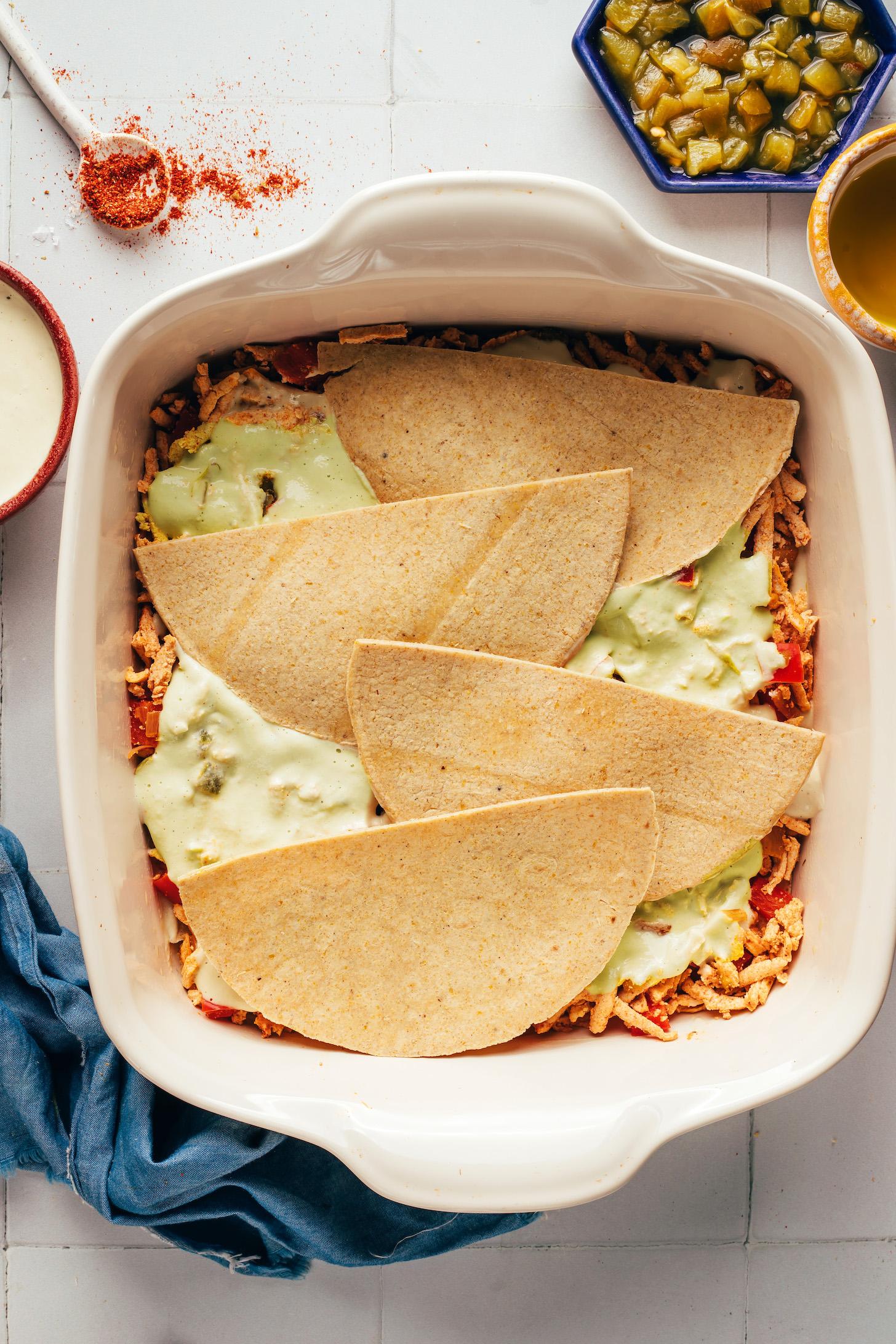 Layers of shredded tofu, creamy cashew sauce, and corn tortillas in a ceramic dish