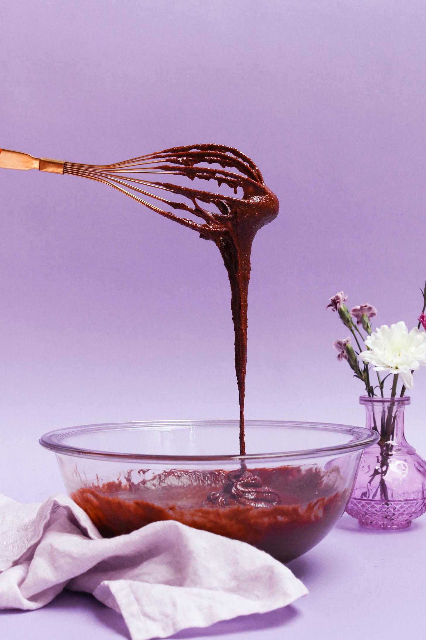 Cake batter dripping from a whisk into a glass mixing bowl