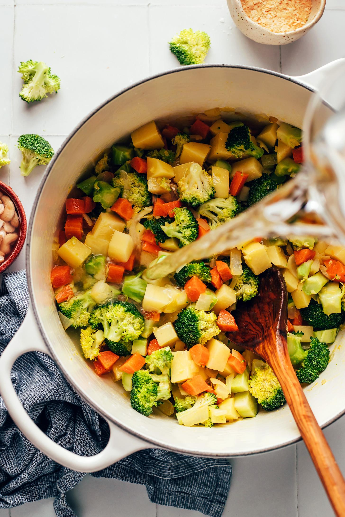 Pouring water into a pot with chopped broccoli, potato, and carrots