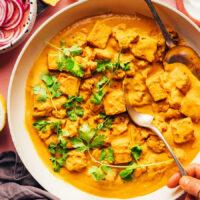 Stirring a skillet of vegan tofu cauliflower korma curry