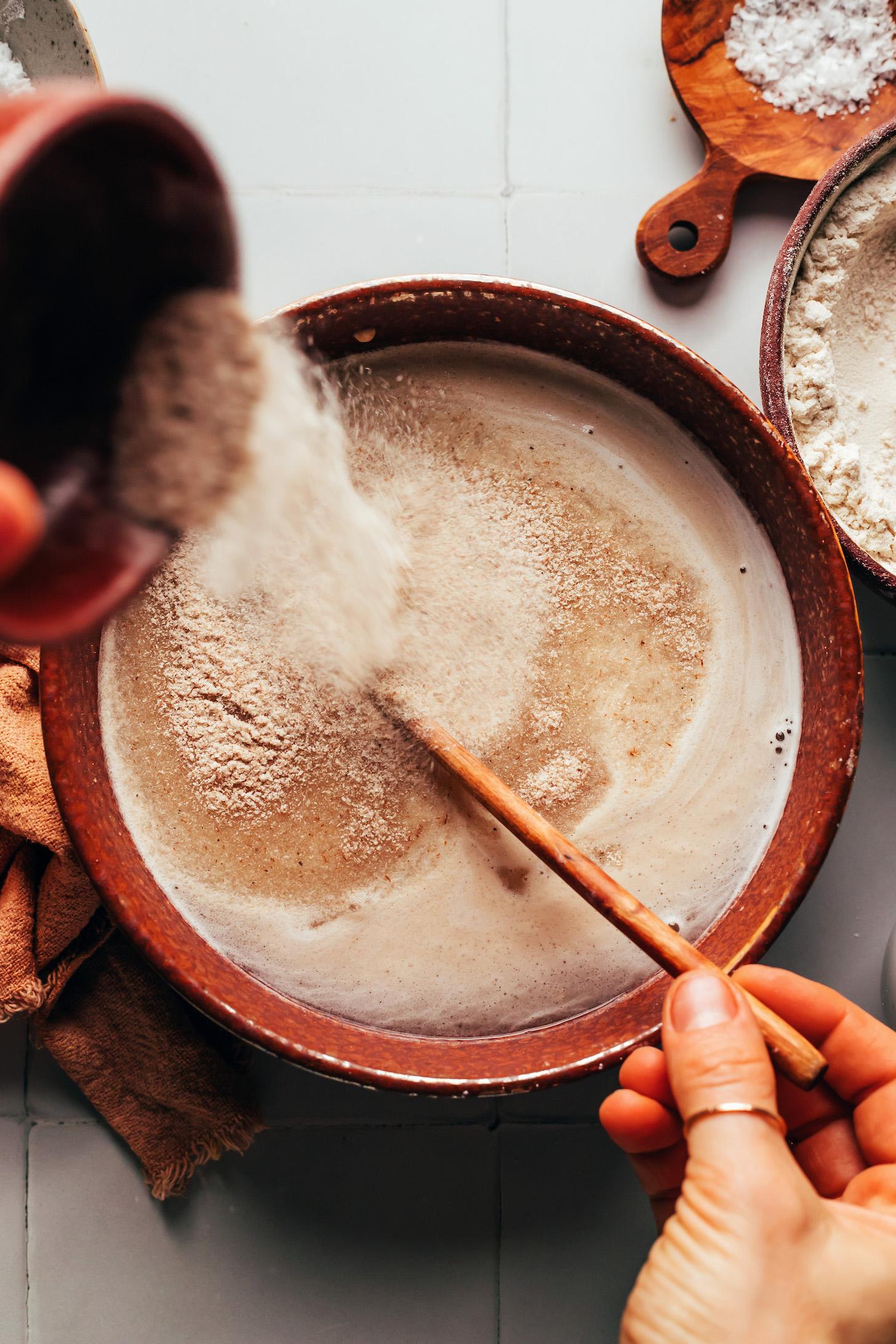 Pouring psyllium husk powder into a bowl of activated yeast water