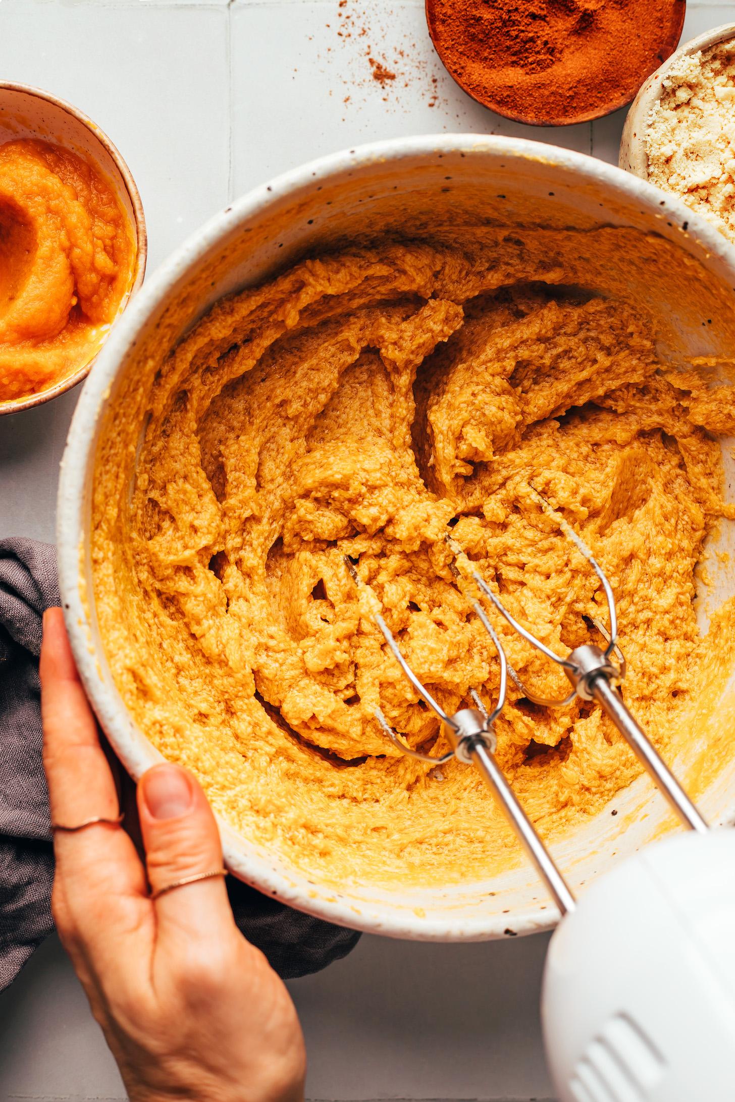 Using an electric mixer to beat cane sugar, vegan butter, pumpkin purée, and vanilla extract