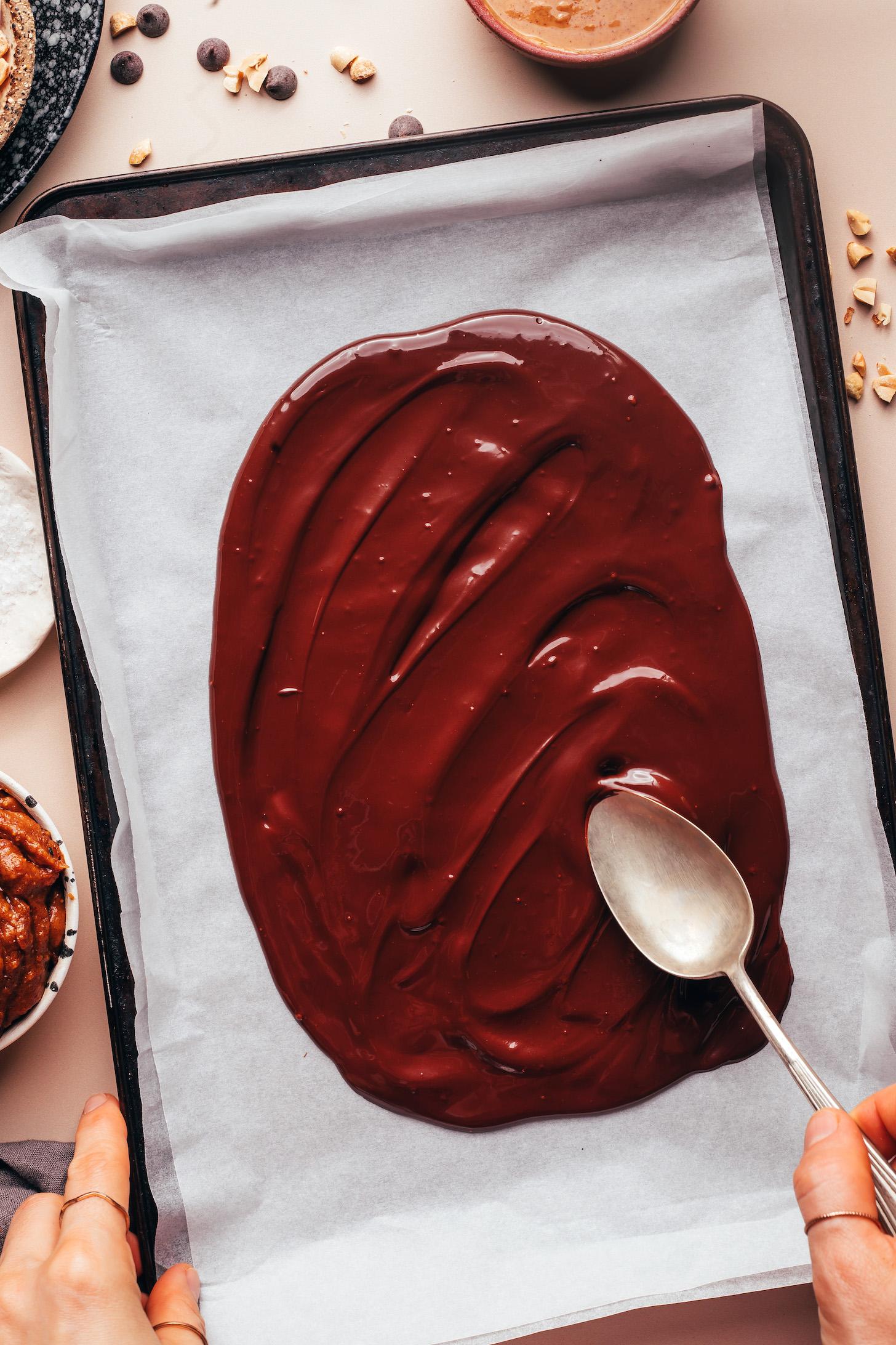 Using a spoon to spread melted chocolate onto a baking sheet