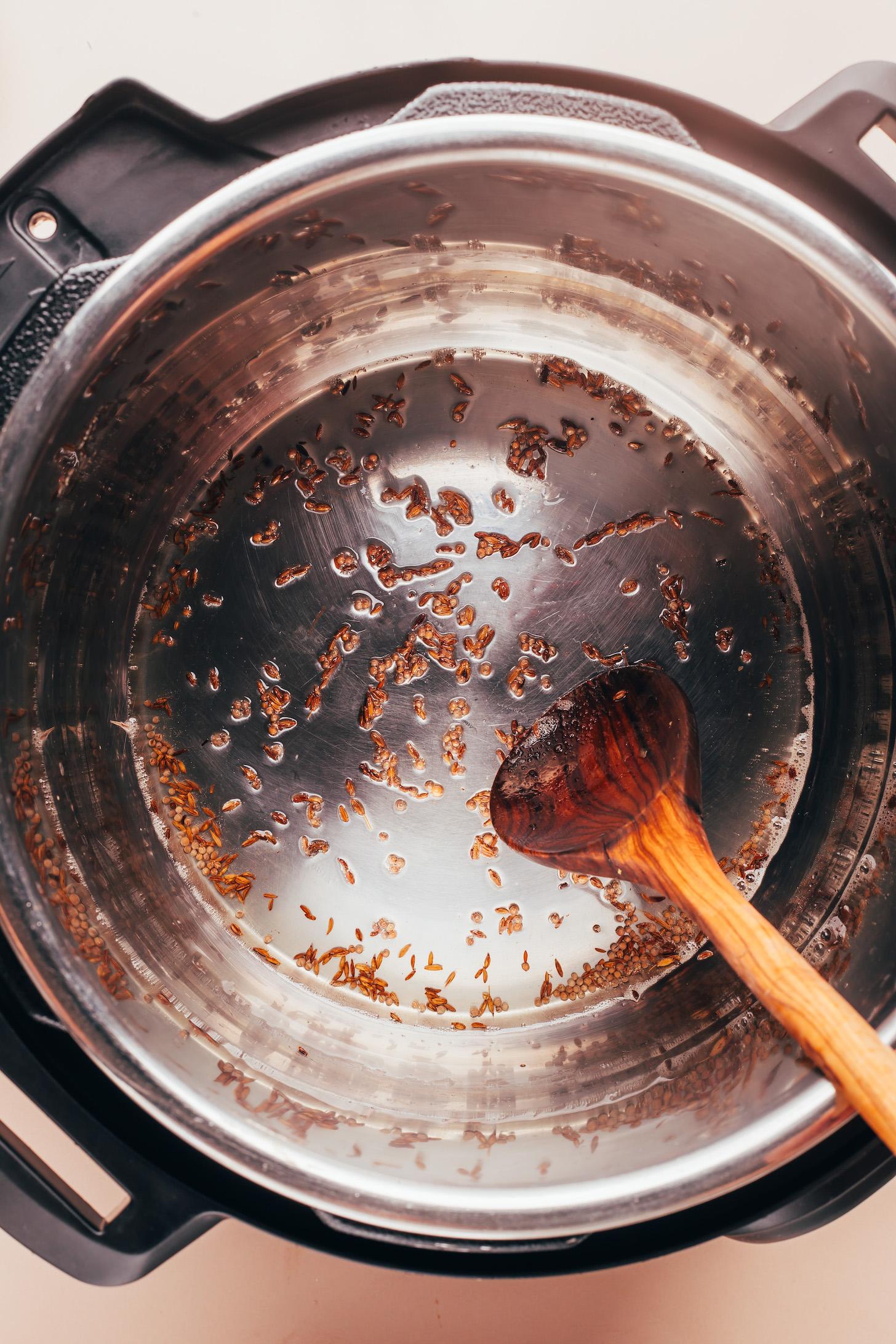 Using a wooden spoon to stir whole spices and melted coconut oil in an Instant Pot before adding rice and water