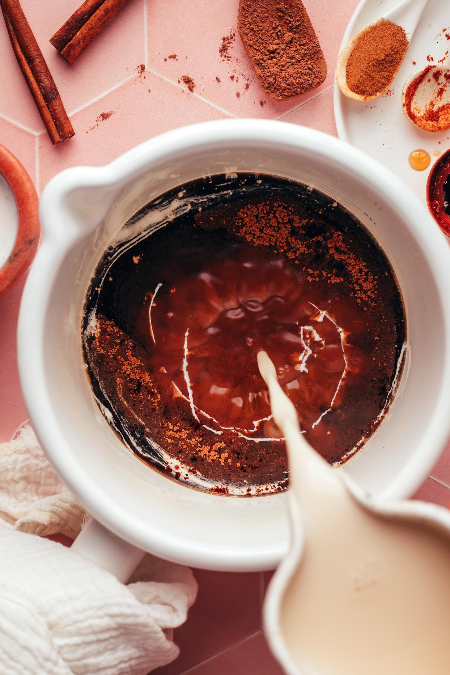 Pouring almond milk into a saucepan with coffee, spices, and sweetener