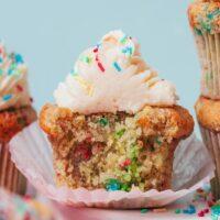 Partially eaten gluten-free funfetti cupcake topped with vanilla buttercream frosting
