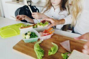 A child and their parent packing a school lunch into a food storage container.