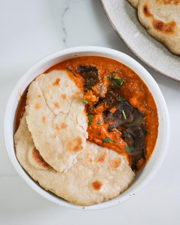 overhead of one serving of vegan butter chicken in a pot next to vegan naan flat bread