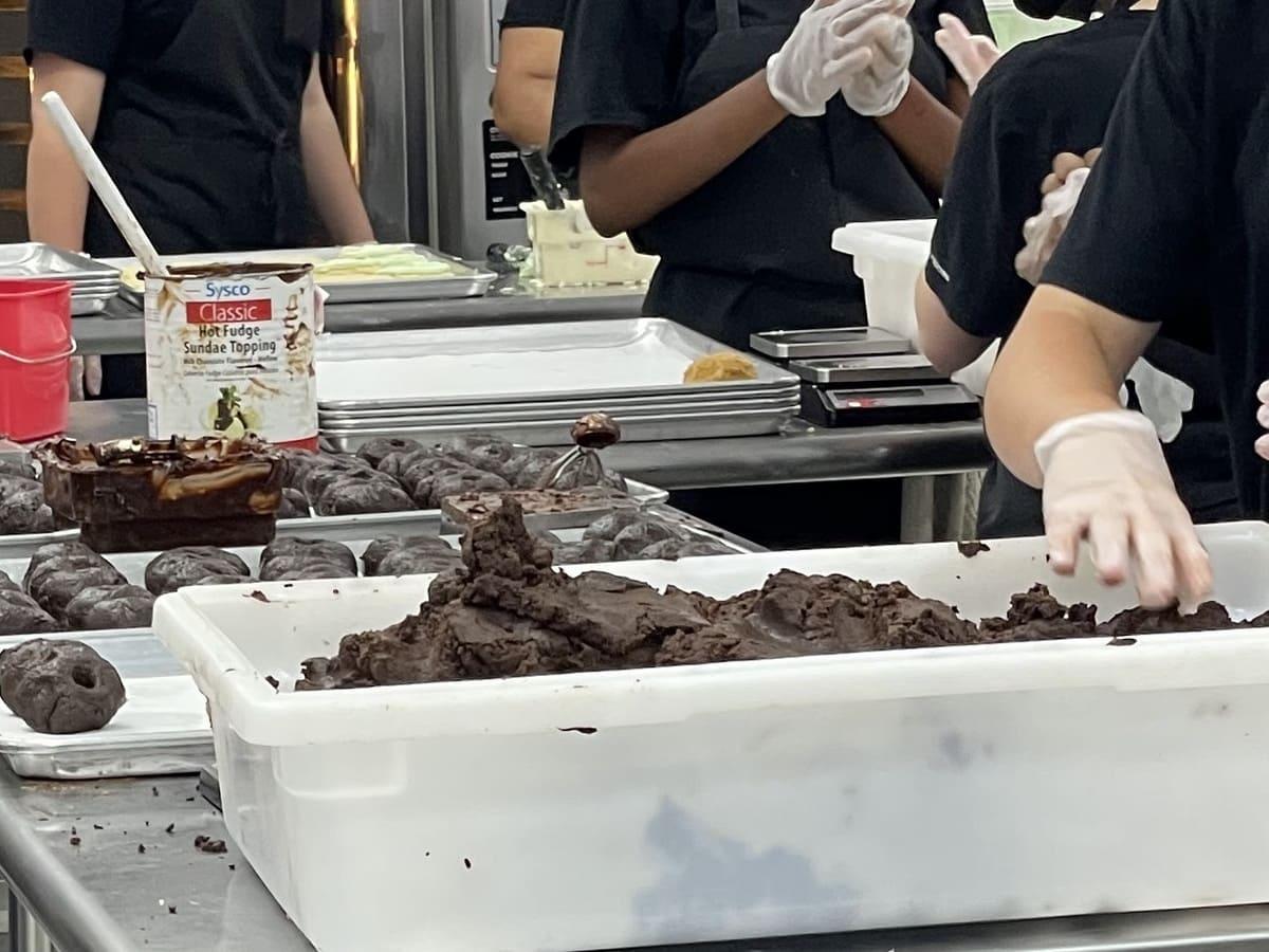 A group of people preparing crumbl cookies in a kitchen.