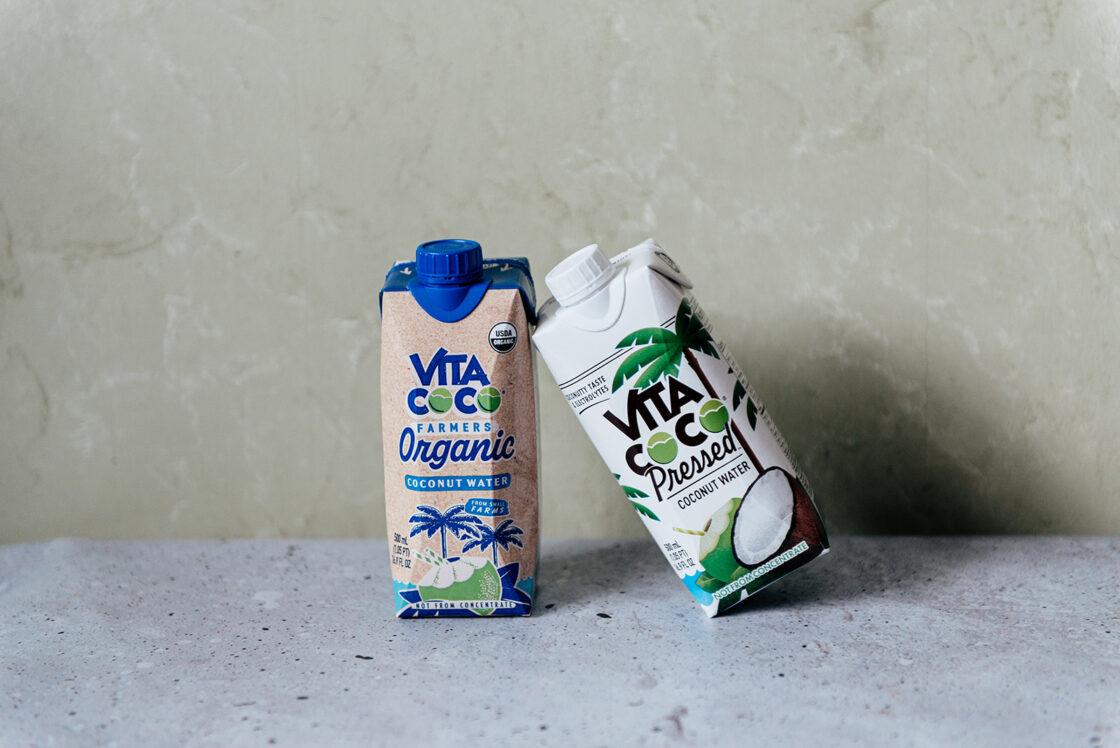 Image of two cartons of Vita Coco coconut water leaning against each other, one is the Farmer's Organic version and the other is the Pressed version.