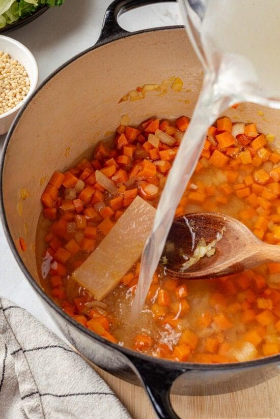 Broth being poured into a pot with carrots