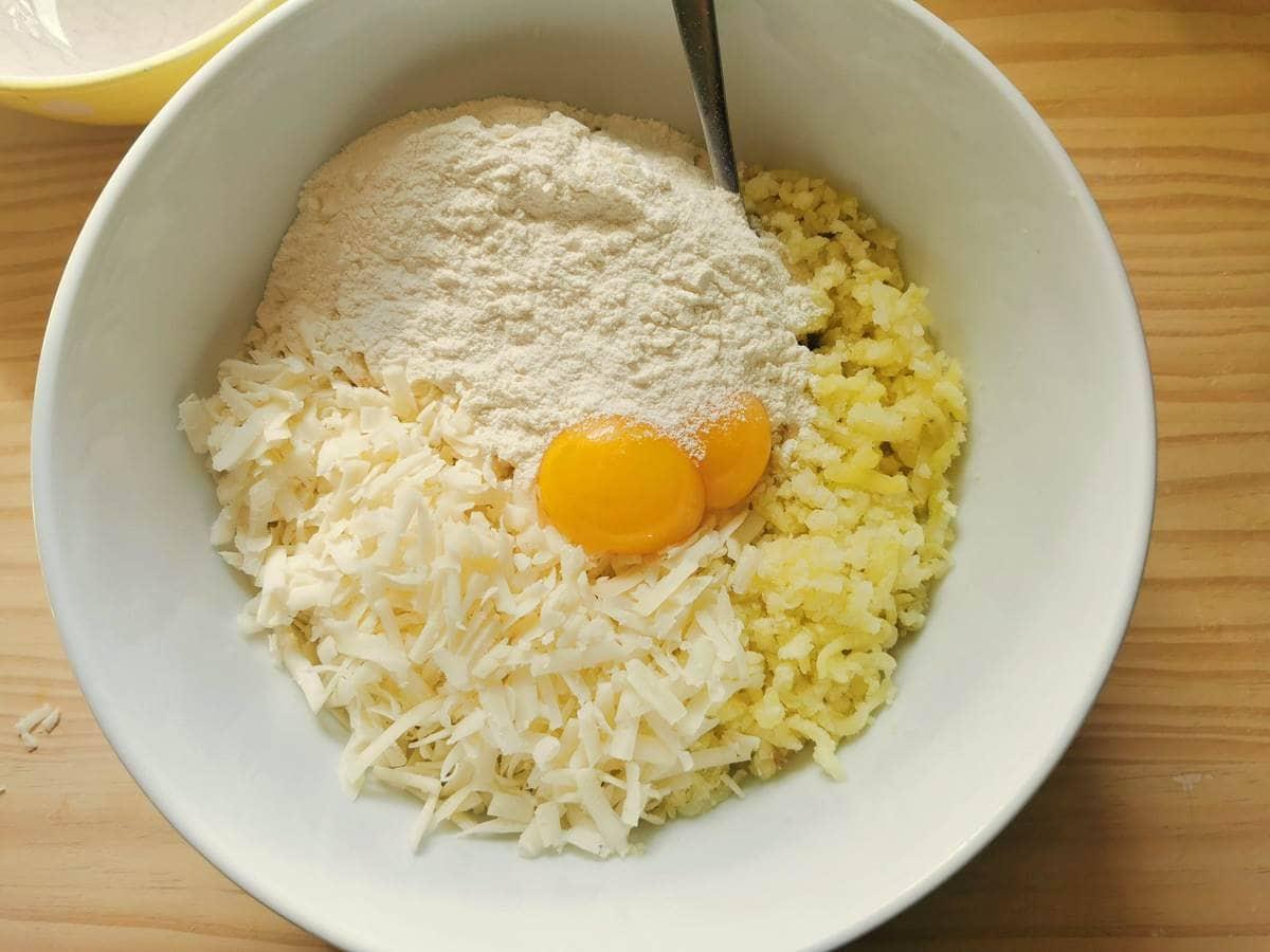 Grated cheese, egg yolks, and flour in large bowl with riced potato.