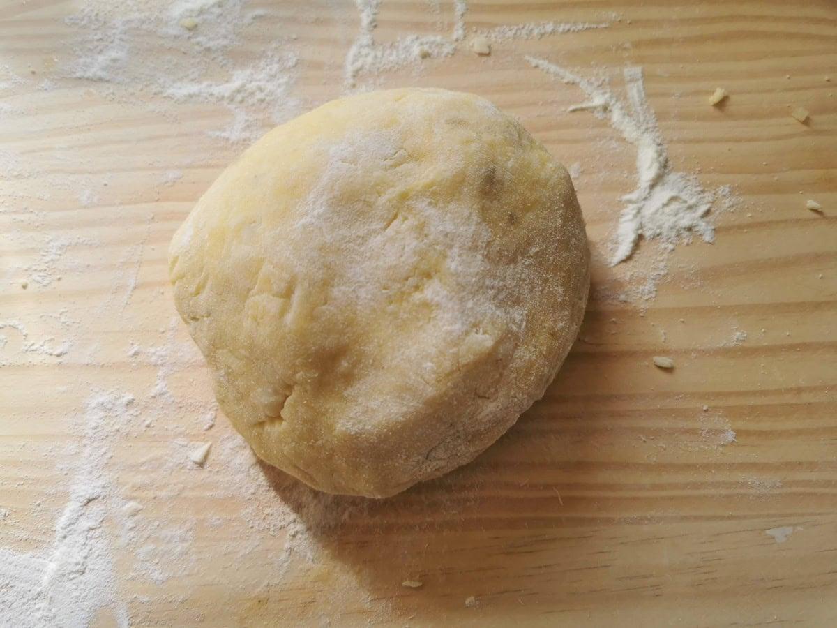 Potato gnocchi dough rolled into a ball on wood work surface.