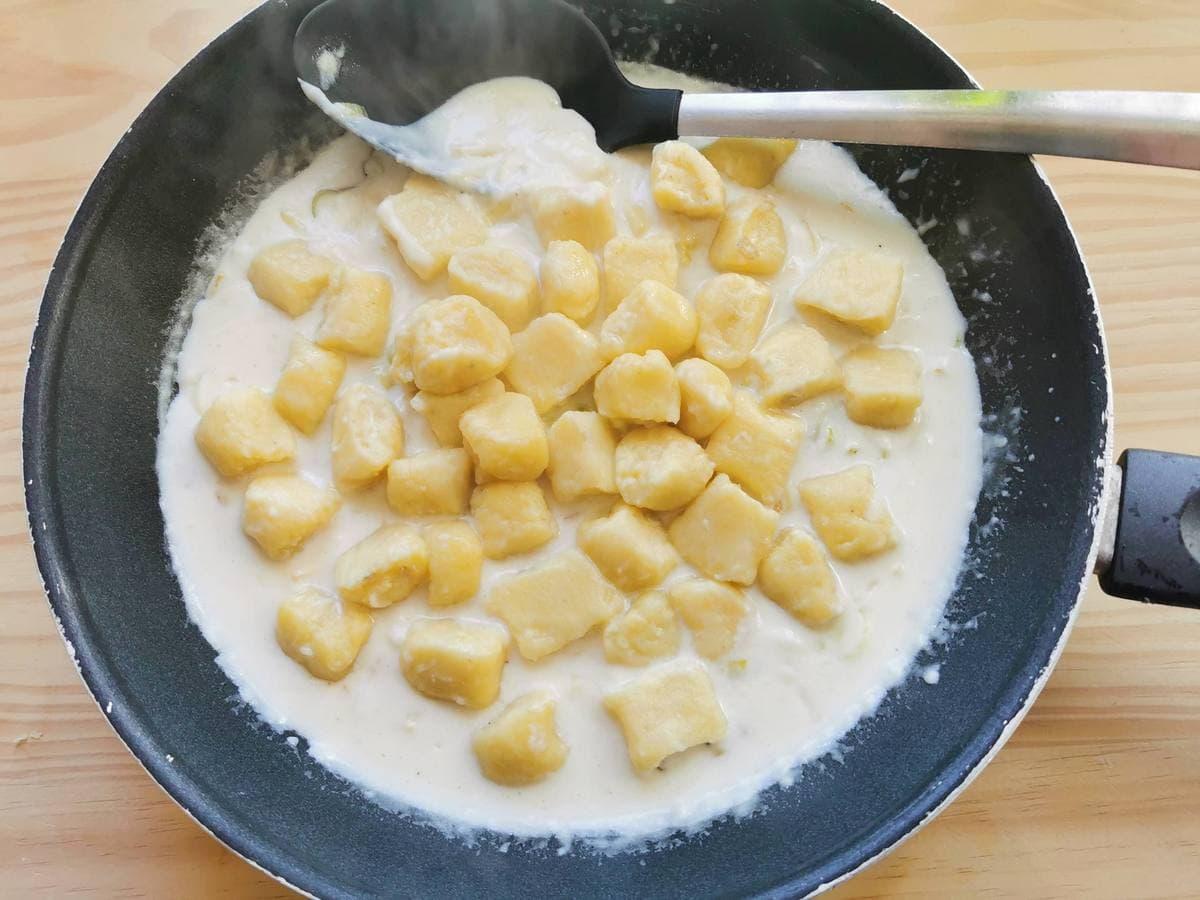 Homemade potato gnocchi in cheese and leek sauce in skillet.