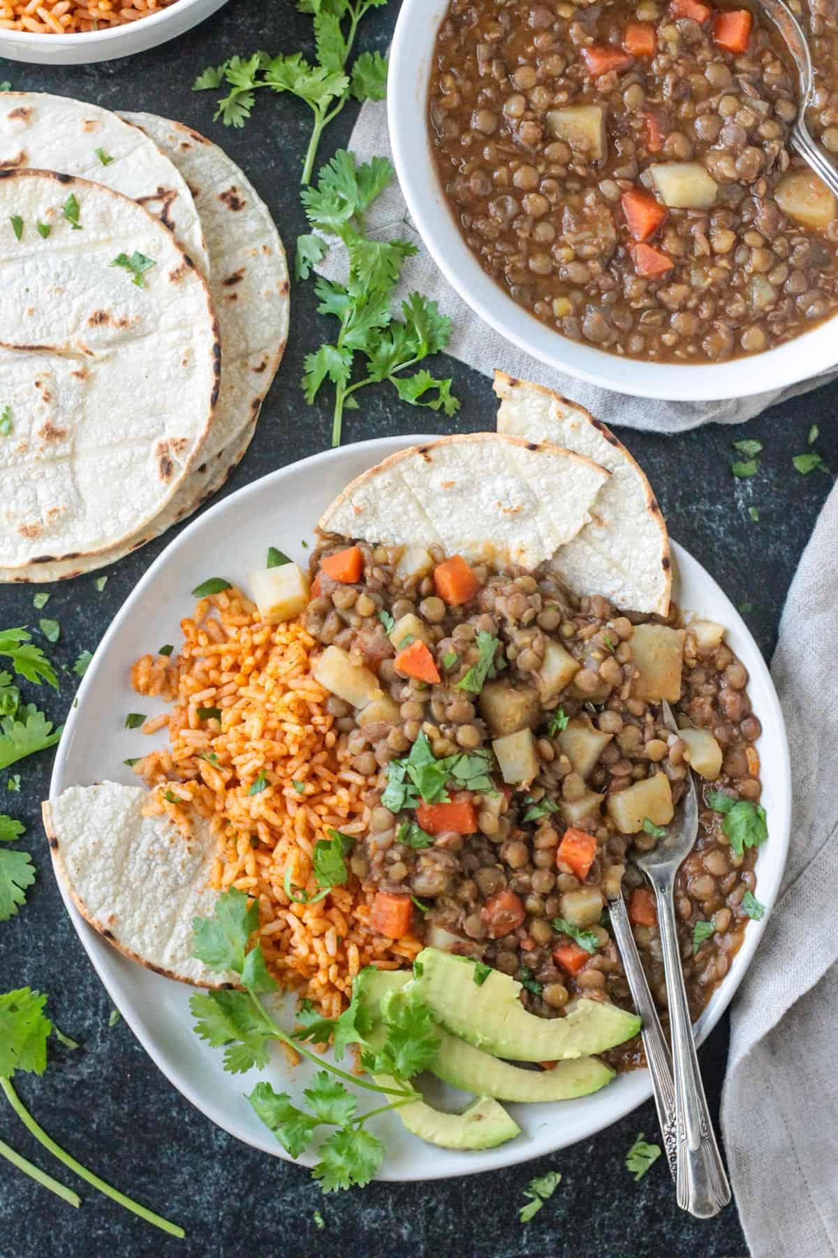 Vegan lentil picadillo on a plate with Mexican red rice, avocado, and corn tortillas.