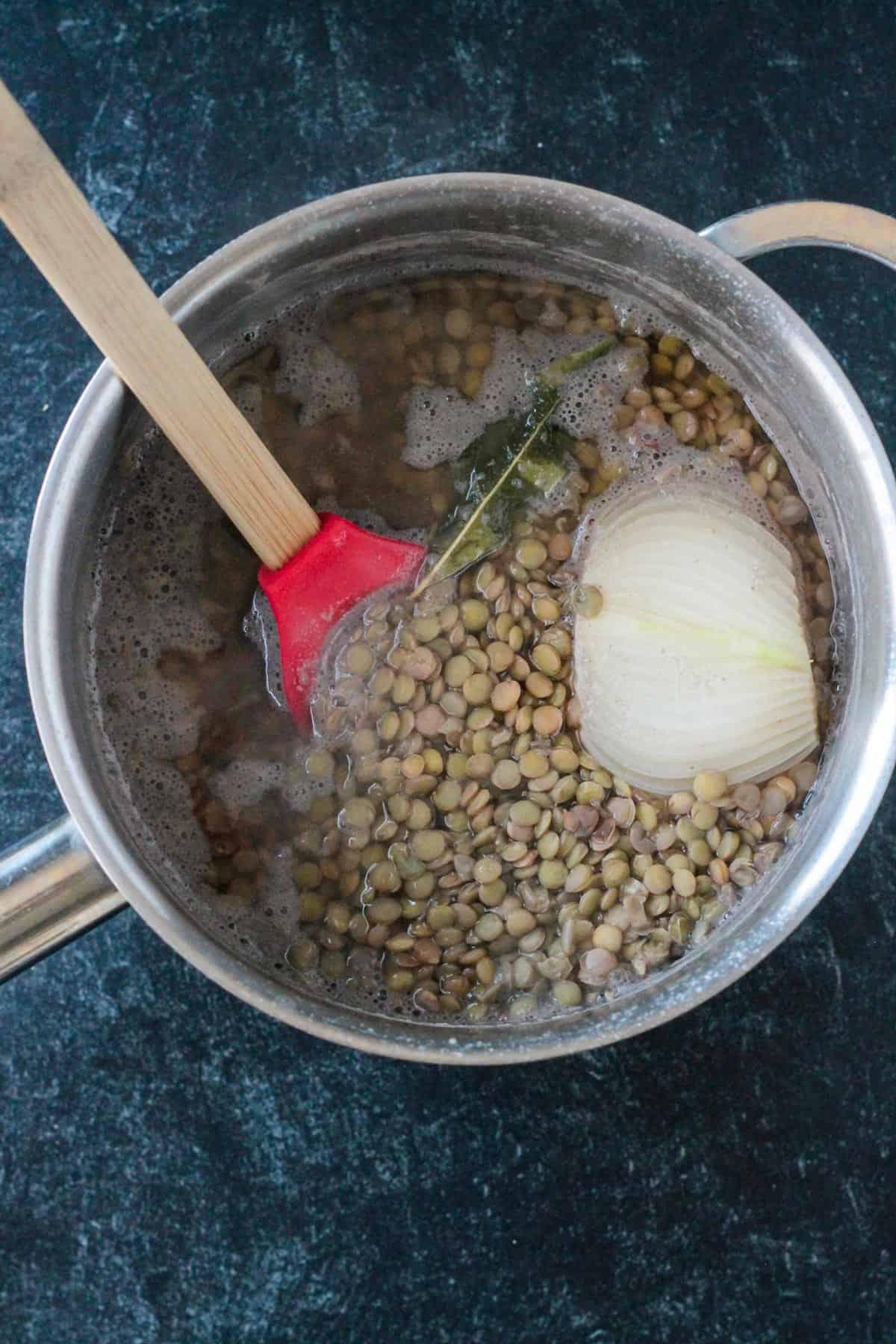 Cooked lentils in a pot with onion and a bay leaf.