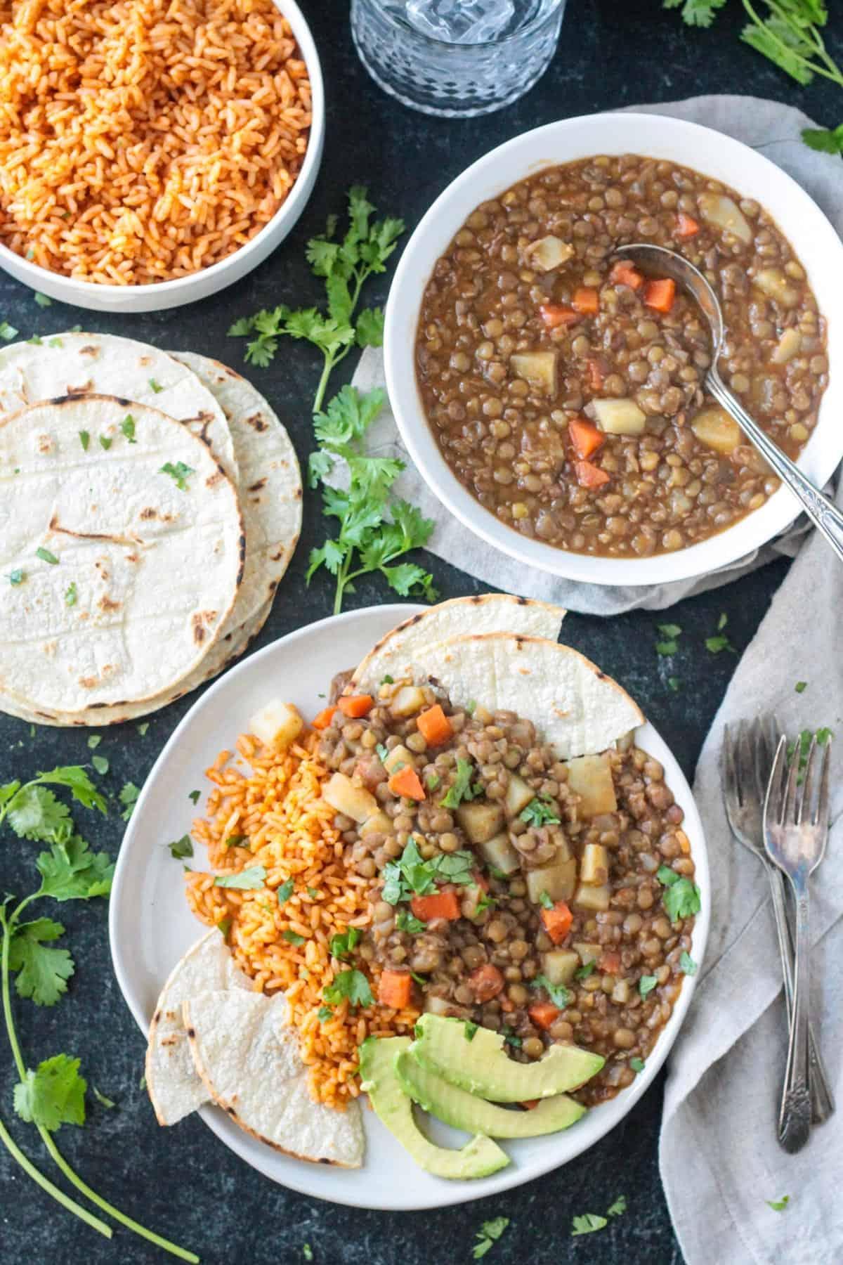 Vegan picadillo on a plate with Mexican rice next a pile of corn tortillas and fresh cilantro.